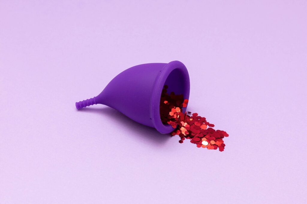 Dream about menstrual blood | Purple menstrual cup with red confetti spilling out of it on pink background.